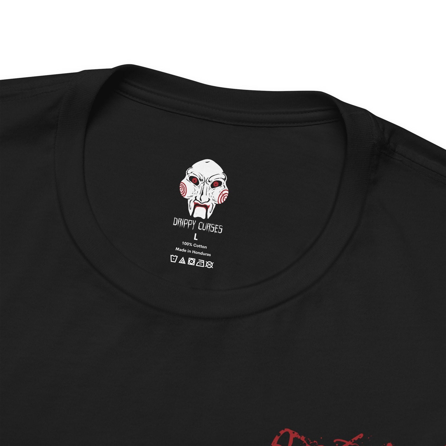 Folded T-Shirt artwork depicting Billy the Puppet emerging from darkness with his tricycle positioned beneath a harsh spotlight. Shadows stretch across the floor while old television screens and mechanical traps fill the background. This design reflects the disturbing symbolism of Jigsaw’s messenger, embodying dread, manipulation, and the cruel tests that define the Saw franchise.